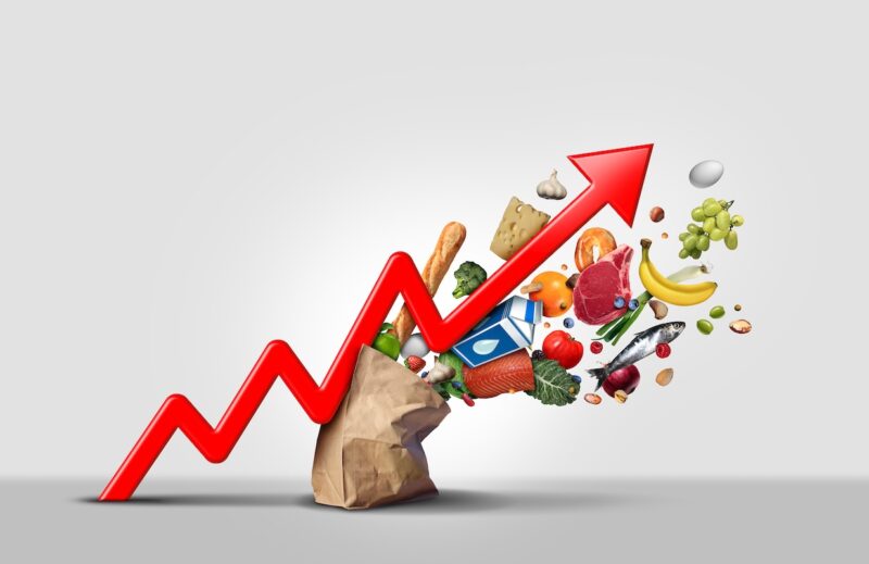 Rising inflation concept with red upward arrow and groceries bursting from a paper bag, representing declining purchasing power and its impact on retirement income planning for investors in the Chicago metro area.