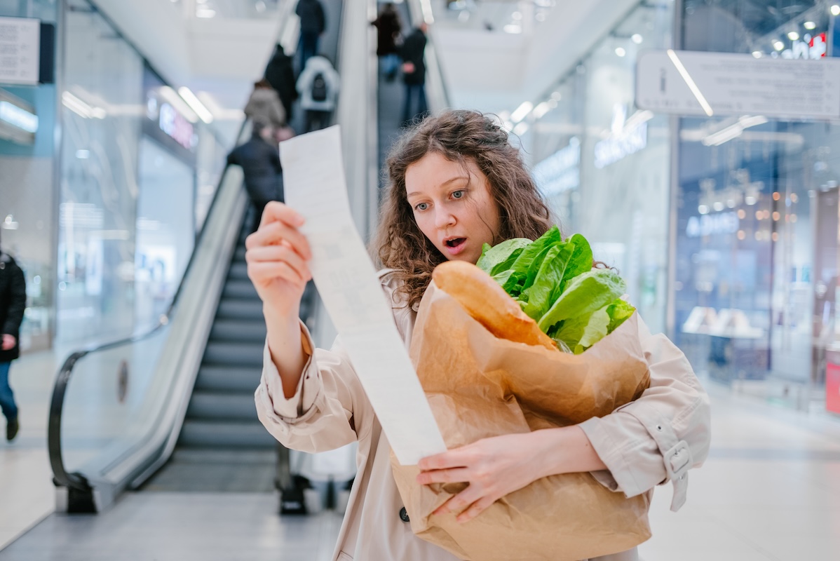Woman reviewing a long grocery receipt while holding groceries in a shopping center, illustrating how rising everyday costs and small inflation assumption errors can impact retirement income planning for pre-retirees and retirees in the Chicago area.