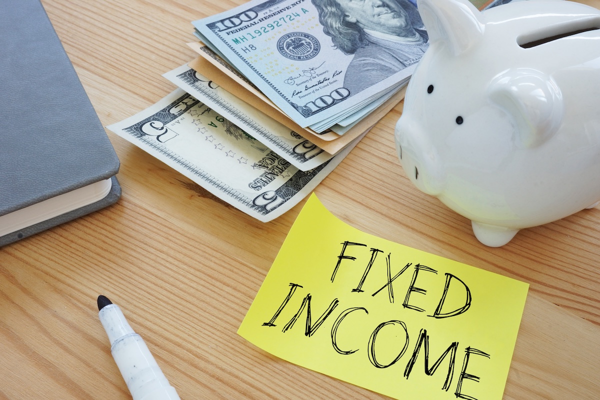 Piggy bank beside cash and a sticky note labeled “fixed income” on a desk, representing inflation-aware fixed income and retirement income planning strategies for retirees and pre-retirees in the Chicagoland area.