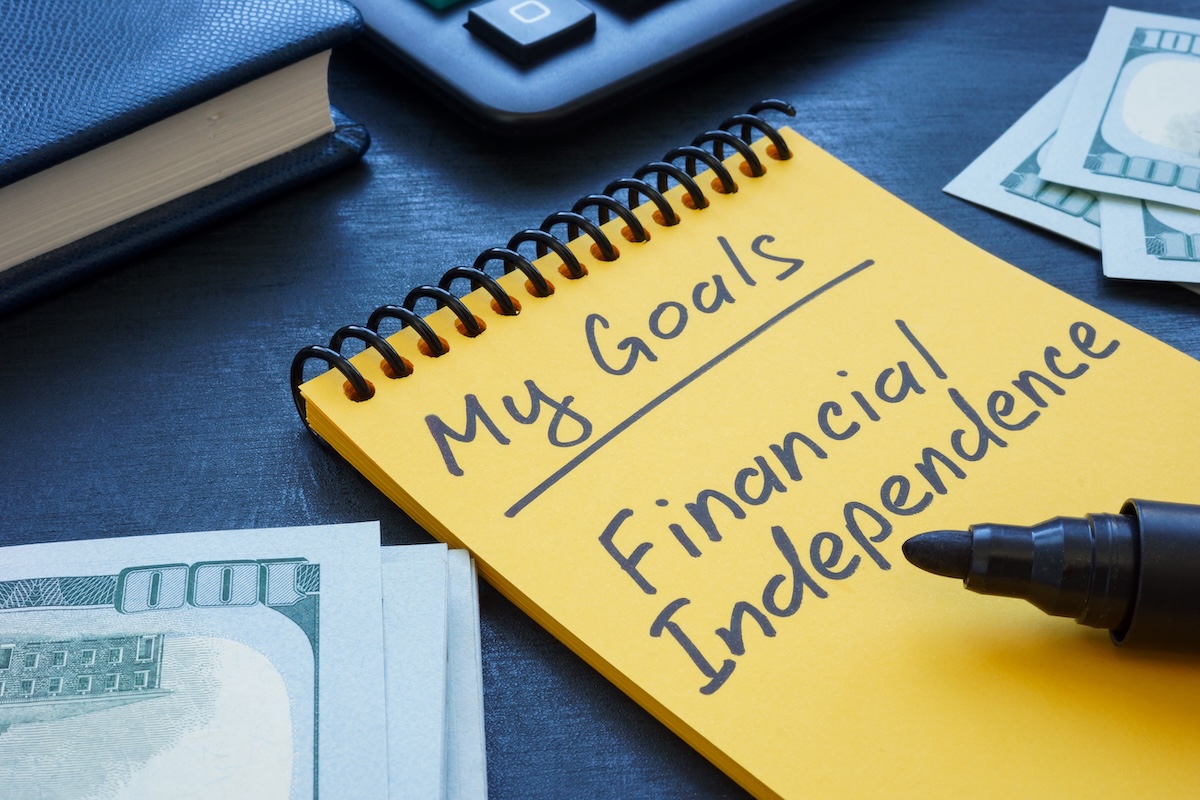 Notebook labeled "My Goals" with the words "Financial Independence" written beside cash, a calculator, and a pen, representing financial planning, retirement planning, wealth management, and achieving financial independence through a personalized financial strategy.